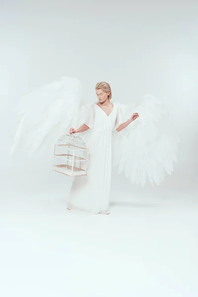 Beautiful woman in angel costume with wings holding bird cage isolated on white — Stock Photo