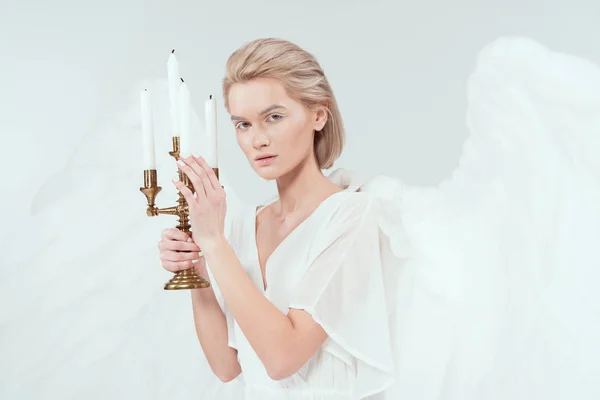 Bela mulher em traje de anjo com asas segurando candelabro com velas e olhando para a câmera isolada no branco — Fotografia de Stock