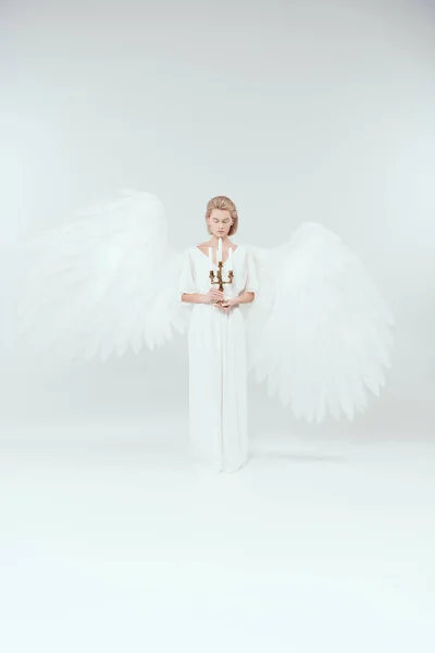 Hermosa mujer en traje de ángel con alas y ojos cerrados sosteniendo candelabro con velas sobre fondo blanco - foto de stock
