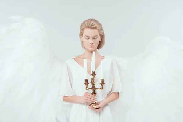 Красива жінка в костюмі ангела з крилами з закритими очима тримає антикварний канделябр ізольований на білому — стокове фото