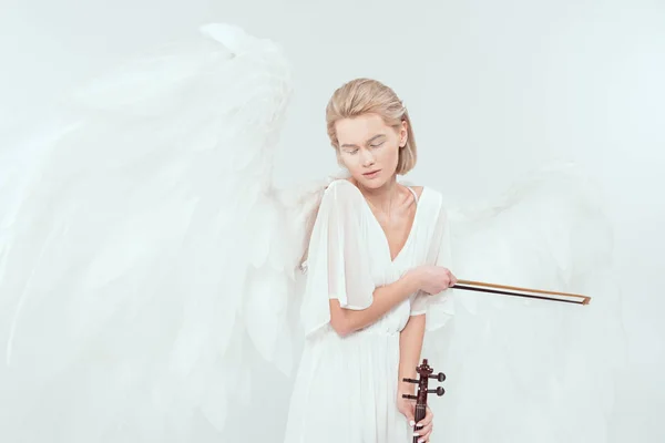 Красива жінка в костюмі ангела з крилами і закритими очима тримає скрипку і лук ізольовано на білому — стокове фото