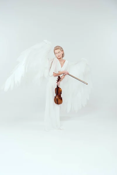 Belle femme en costume d'ange avec des ailes tenant violon et arc isolé sur blanc — Photo de stock