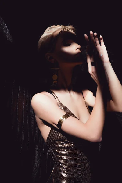 Красива сексуальна жінка з ангельськими крилами і золотими аксесуарами позує і жестикулює руками ізольовано на чорному — стокове фото