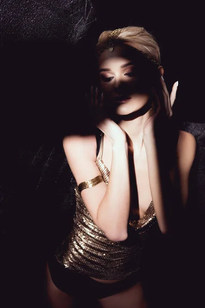 Schöne Frau in goldenen Accessoires gestikuliert mit den Händen und posiert auf schwarzem Hintergrund — Stockfoto