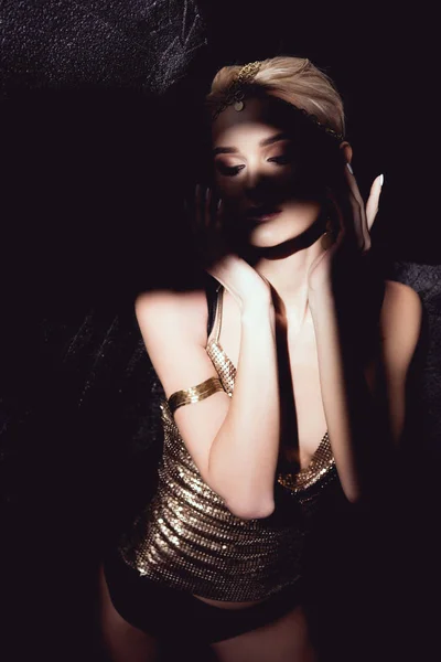 Beautiful woman in golden accessories gesturing with hands and posing on black background — Stock Photo