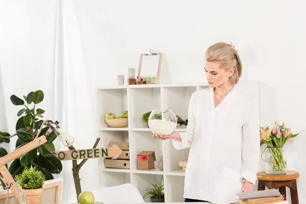 Attraente donna guardando ciotola di vetro pesce con sabbia vicino andare segno verde in ufficio, concetto di risparmio ambientale — Foto stock