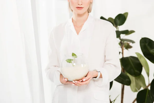 Cropped view of woman holding glass fish bowl with sand near and green leaves,  environmental saving concept — Stock Photo