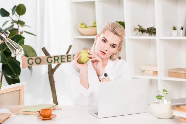 Attraente donna in possesso di mela verde e seduto vicino andare segno verde, concetto di risparmio ambientale — Foto stock