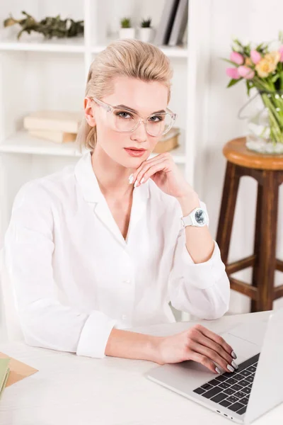 Attractive woman in glasses sitting near laptop in office — Stock Photo