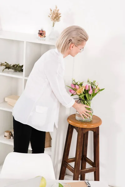 Woman looking at flowers in vase in modern office — Stock Photo