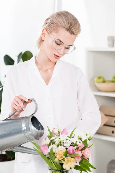 Schöne Geschäftsfrau mit Gießkanne und Blumen in der Vase, Umweltschutzkonzept — Stockfoto