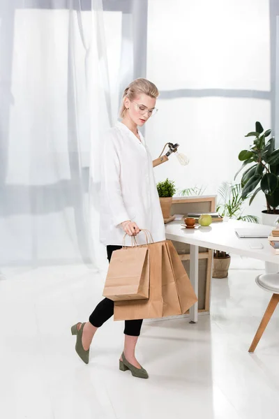Mulher bonita em óculos andando com sacos de compras no escritório — Fotografia de Stock