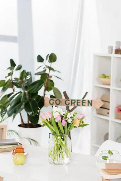 Selective focus of flowers in glass vase near wooden sign with go green lettering on background, environmental saving concept — Stock Photo