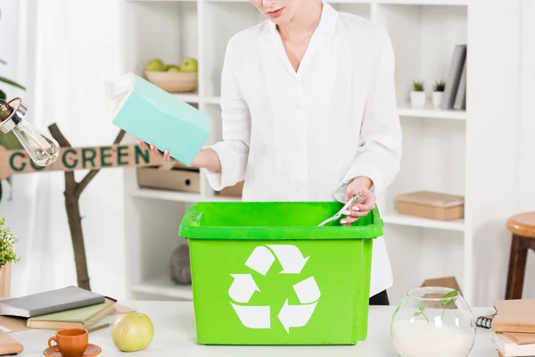 Vue recadrée de la femme tenant le paquet de lait près de la boîte de recyclage tout en restant au bureau, concept d'économie de l'environnement — Photo de stock