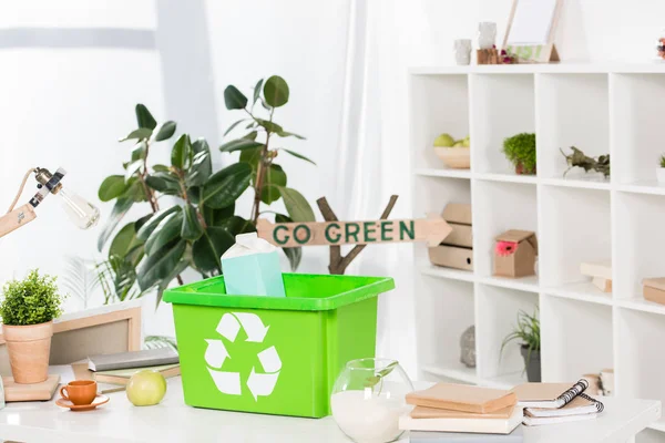 Focus selettivo della scatola di riciclaggio verde con pacchetto di latte di carta sulla scrivania con segno go green sullo sfondo, concetto di risparmio ambientale — Foto stock