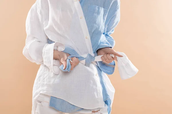 Vue recadrée d'une femme nouant un nœud debout dans des vêtements éco isolés sur beige — Photo de stock