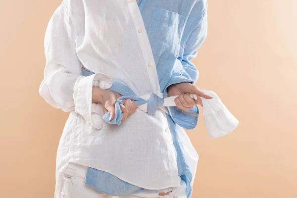 Cropped view of woman tying knot while standing in eco clothing isolated on beige — Stock Photo