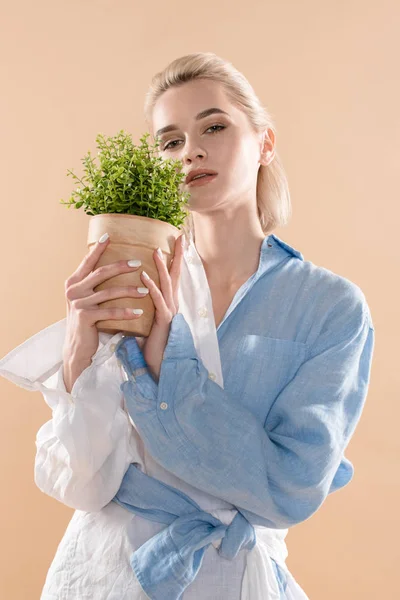 Bela mulher segurando panela com planta e de pé em eco vestuário isolado em bege, conceito de poupança ambiental — Fotografia de Stock