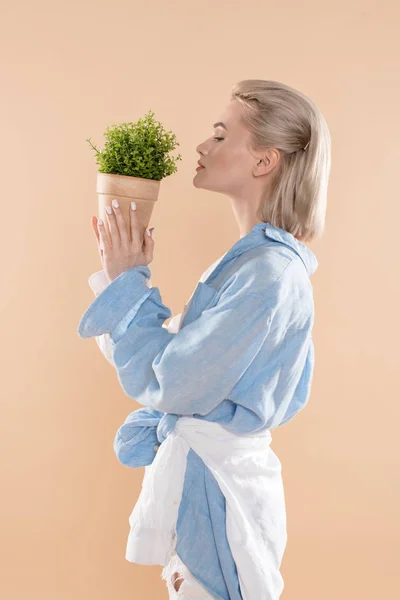 Profile of woman holding pot with plant and standing in eco clothing isolated on beige, environmental saving concept — Stock Photo