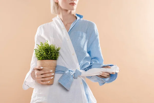 Abgeschnittene Ansicht einer Frau, die einen Topf mit Pflanze hält und in Öko-Kleidung isoliert auf beige steht, Umweltschutzkonzept — Stockfoto