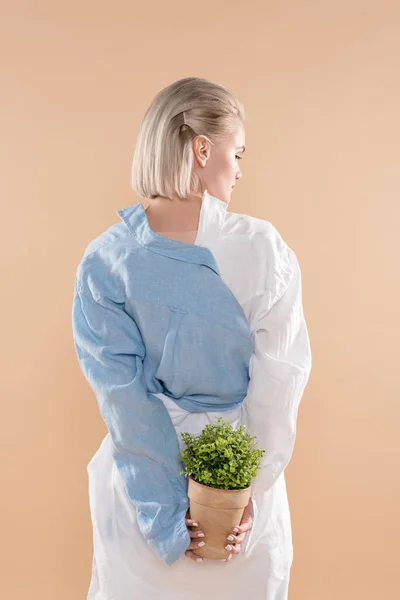 Молода жінка тримає горщик з рослиною ізольовано на бежевому, концепція екологічної економії — стокове фото