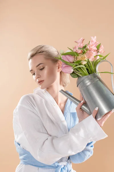 Femme tenant arrosoir avec des fleurs et debout dans des vêtements écologiques isolés sur beige, concept d'économie de l'environnement — Photo de stock