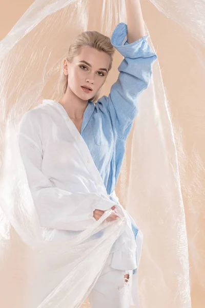 Mujer sosteniendo polietileno mientras está de pie en la ropa ecológica aislado en beige, concepto de ahorro ambiental - foto de stock