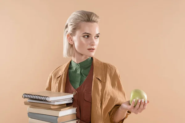 Attraktives Mädchen mit Büchern und grünem Apfel, während es in Öko-Kleidung isoliert auf beige steht — Stockfoto