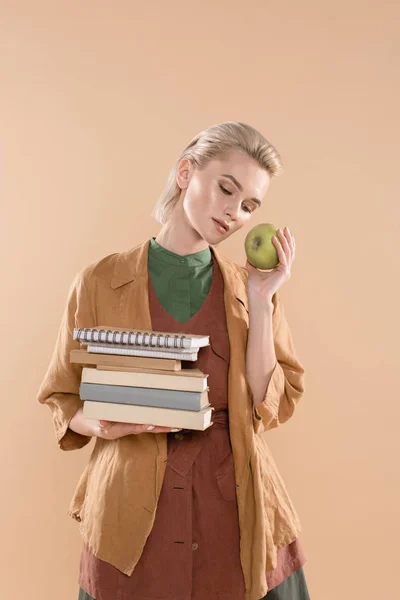 Attraktive junge Frau mit Büchern und grünem Apfel, während sie in Öko-Kleidung isoliert auf Beige steht — Stockfoto