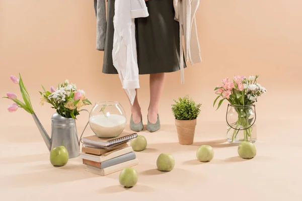 Vista recortada de la mujer sosteniendo ropa ecológica cerca de plantas y flores sobre fondo beige, concepto de ahorro ambiental - foto de stock