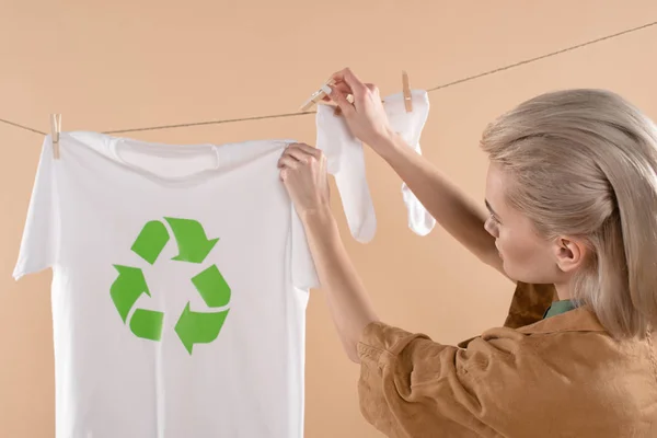 Mujer rubia entregando calcetines blancos cerca de camiseta con cartel de reciclaje en tendedero aislado en beige, concepto de ahorro ambiental - foto de stock