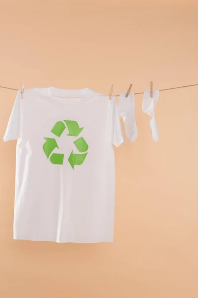 White socks near t-shirt with recycling sign on clothesline isolated on beige, environmental saving concept — Stock Photo