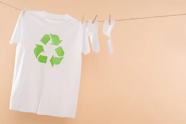 T-Shirt mit Recyclingschild an der Wäscheleine in der Nähe weißer Socken isoliert auf beige, Umweltschutzkonzept — Stockfoto