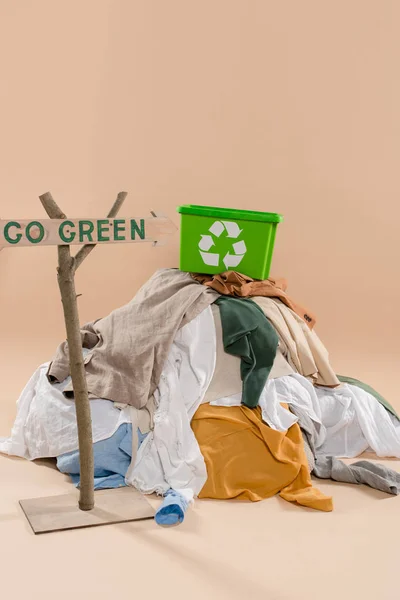 Wooden sign with go green lettering near recycling box on pile of clothing on beige background, environmental saving concept — Stock Photo