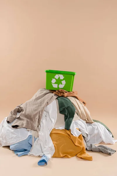 Recycling box on stack of clothing on beige background, environmental saving concept — Stock Photo