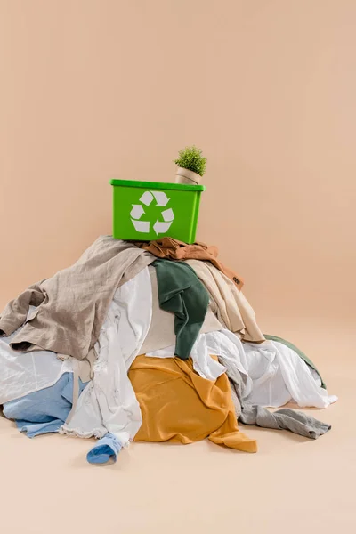 Scatola di riciclaggio verde con impianto in vaso su pila di abbigliamento su sfondo beige, concetto di risparmio ambientale — Foto stock