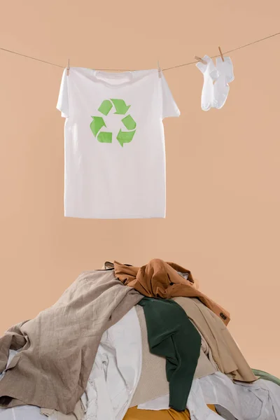 T-Shirt mit Recyclingschild an der Wäscheleine in der Nähe weißer Socken und Kleiderstapel auf beigem Hintergrund, Umweltschutzkonzept — Stockfoto