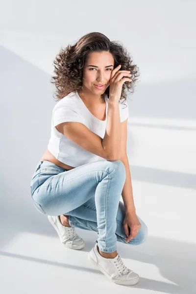 Attractive brunette girl in jeans sitting on grey background — Stock Photo
