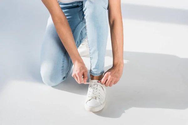 Partial view of woman in jeans tying shoelaces — Stock Photo