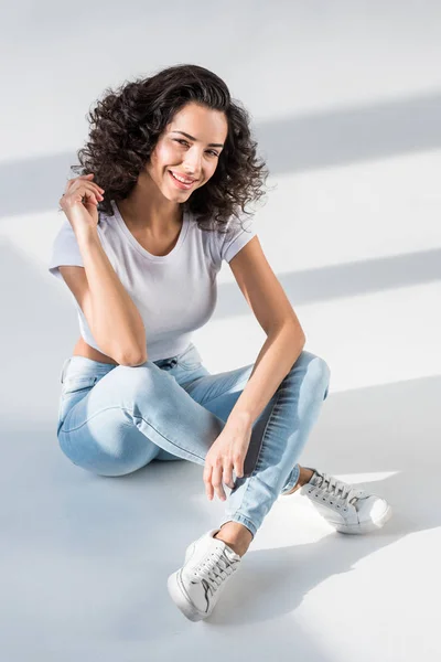 Laughing curly girl in jeans sitting on floor and looking at camera — Stock Photo