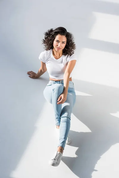 Curious young woman in jeans sitting on floor — Stock Photo