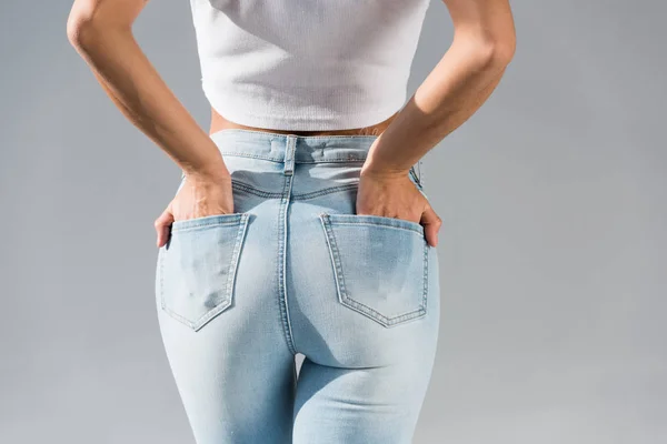 Abgeschnittene Ansicht einer jungen Frau in Jeans mit Händen in Taschen isoliert auf grau — Stockfoto