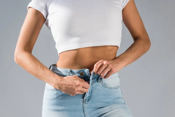 Vista parcial de la mujer sexy desabrochando jeans aislados en gris - foto de stock