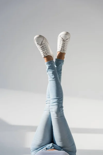 Vue recadrée d'une femme en jean bleu posant avec des jambes croisées sur fond gris — Photo de stock