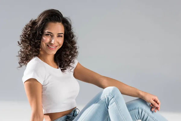 Laughing curly woman in crop top sitting on grey background — Stock Photo