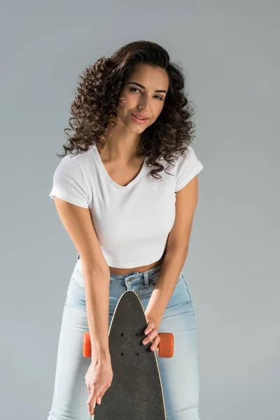 Curieux brunette fille tenant longboard isolé sur gris — Photo de stock