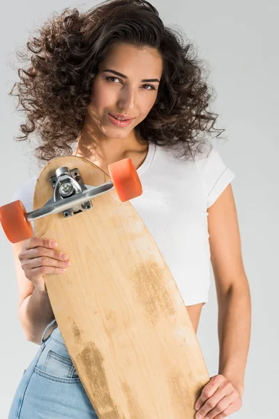 Attractive curly girl holding wooden longboard on grey background — Stock Photo