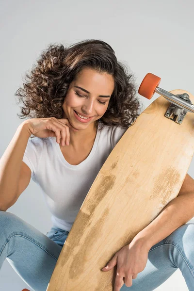 Dreamy curly girl holding longboard on grey background — Stock Photo