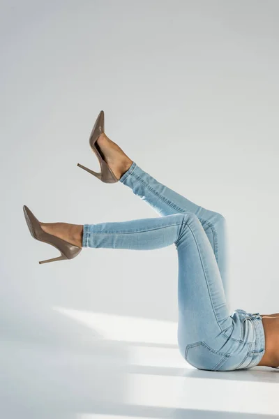 Vista parcial de mulher em jeans azul e sapatos de salto alto em fundo cinza — Fotografia de Stock