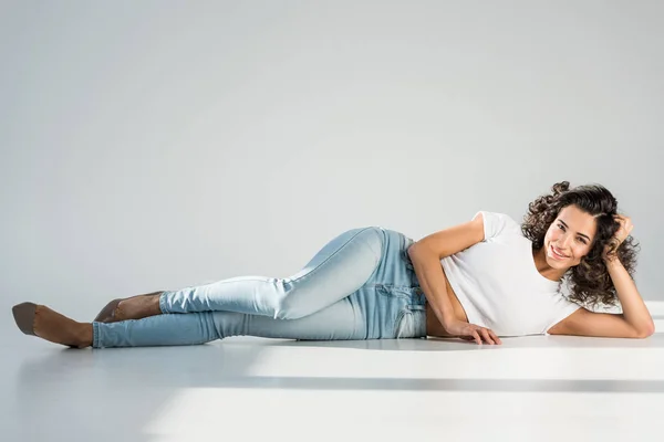 Чудова молода жінка в джинсах лежить на сірому фоні — стокове фото